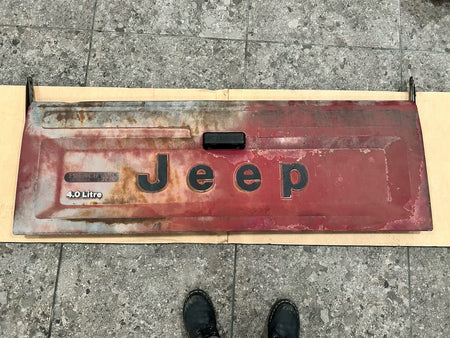 Jeep Comanche tailgate showing weathered red surface and large black lettering, highlighting the model's 4.0 Litre feature.